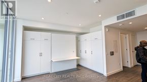 Kitchener condo for rent - A man is standing in a room with white cabinets and a doorway leading to another room.