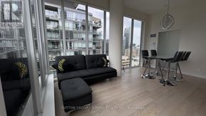 Toronto (Church-Yonge Corridor) condo for rent - A black couch with gold pillows sits in a room with a view of a cityscape.