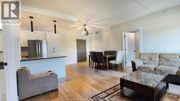 Lasalle condo for rent - A living room with a grey couch, a dining table with chairs, and a kitchen area with a refrigerator and stove.