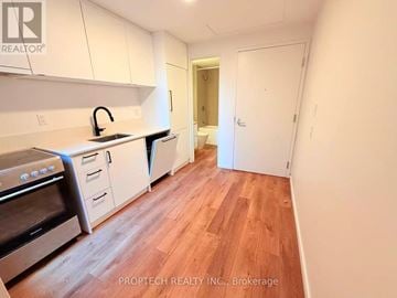 Toronto (North Riverdale) multi-family for rent - A kitchen with white cabinets and wood flooring.