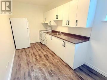 Toronto (North Riverdale) multi-family for rent - A kitchen with white cabinets and a white refrigerator.