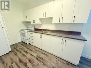 Toronto (North Riverdale) multi-family for rent - A kitchen with white cabinets and a wooden floor.