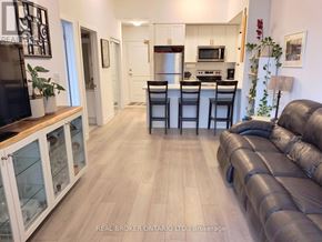 Hamilton (Waterdown) condo for rent - A living room with a black leather couch and a kitchen area in the background.