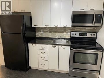 Welland apartment for rent - A black refrigerator is in a kitchen with white cabinets.