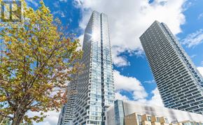 Vaughan (Vaughan Corporate Centre) condo for rent - A tall building with a glass facade stands in front of a tree with yellow leaves.