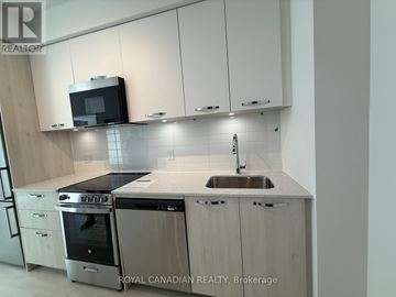 Hamilton (Corktown) condo for rent - A kitchen with white cabinets and a black microwave above the stove.