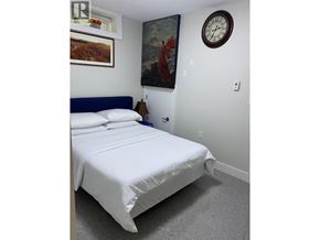Vancouver apartment for rent - A bed with white sheets and a blue headboard is in a room with a clock on the wall.