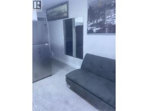 Vancouver apartment for rent - A grey couch sits in a room with a fridge and a picture on the wall.