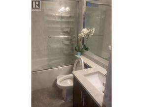 Vancouver apartment for rent - A white toilet is in a bathroom with a sink and a vase of flowers.