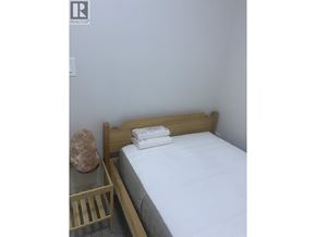 Vancouver apartment for rent - A bed with white sheets and a wooden headboard sits next to a nightstand with a rock on top.