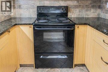 Calgary apartment for rent - A black oven with a stainless steel handle is in a kitchen with wooden cabinets.