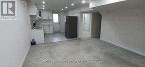 Clarington (Bowmanville) apartment for rent - A spacious room with a kitchen area in the background and a refrigerator in the foreground.