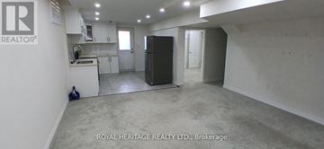 Clarington (Bowmanville) apartment for rent - A spacious room with a kitchen area in the background and a refrigerator in the foreground.