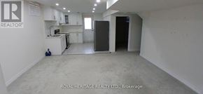 Clarington (Bowmanville) apartment for rent - A spacious, empty room with white walls and a kitchen area in the background.