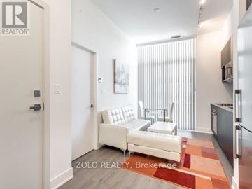 Toronto (Banbury-Don Mills) condo for rent - A white couch sits in a modern living room with a kitchen area in the background.