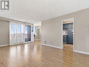 Ajax (Central West) condo for rent - A spacious room with wooden flooring and a kitchen area in the background.