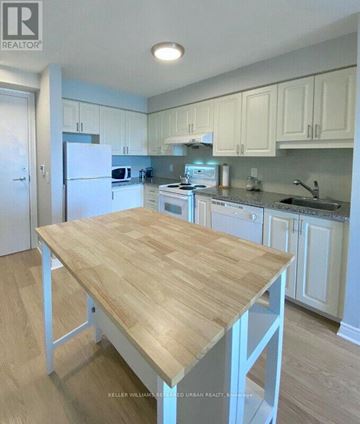 Toronto (Bendale) condo for rent - A kitchen with a table in the middle and cabinets above.