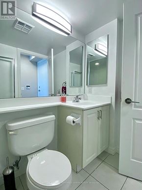 Toronto (Bendale) condo for rent - A white toilet in a small bathroom with a sink and mirror.