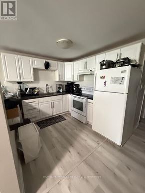 Mississauga (Streetsville) multi-family for rent - A white refrigerator stands in a kitchen with white cabinets and a black countertop.