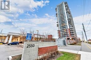 Oshawa (Windfields) condo for rent - A tall residential building stands next to a sign for a realtor.