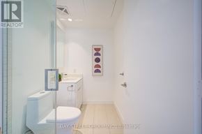 Toronto (Bay Street Corridor) condo for rent - A white toilet sits in a small bathroom with a framed picture on the wall.