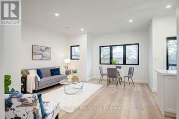 Stratford multi-family for rent - A well-lit living room with a grey sofa, a coffee table, and a dining table with chairs.