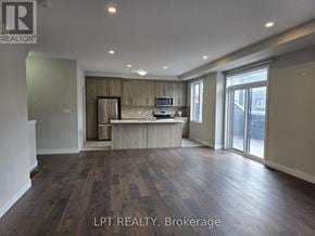 London East (East D) townhouse for rent - A spacious living room with wood flooring and a kitchen area in the background.