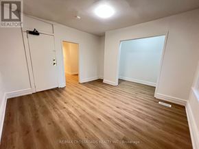 Toronto (South Riverdale) apartment for rent - A room with wooden flooring and white walls, with a door on the left and a large window on the right.