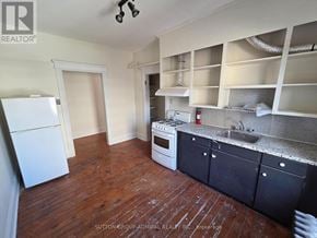 Toronto (Yonge-St. Clair) fourplex for rent - A kitchen with a white fridge, black cabinets, and a wooden floor.
