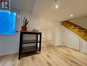 Toronto (Trinity-Bellwoods) townhouse for rent - A room with a wooden floor and a staircase in the background.