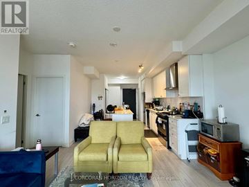 Kitchener condo for rent - A living room with a yellow couch and a kitchen area in the background.
