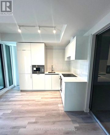 Toronto (Kensington-Chinatown) condo for rent - A modern kitchen with white cabinets and a wooden floor.