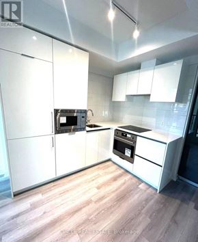 Toronto (Kensington-Chinatown) condo for rent - A modern kitchen with white cabinets and a wooden floor.