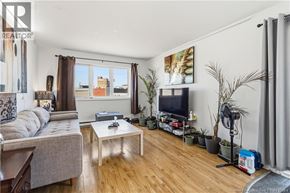 Moncton multi-family for rent - A living room with a grey sofa, a white coffee table, and a TV on the wall.