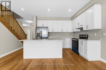 Clarington (Bowmanville) townhouse for rent - A modern kitchen with white cabinets and a wooden staircase.