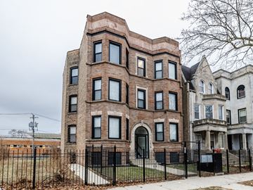 Chicago apartment for rent - A large brick building with a black fence in front.