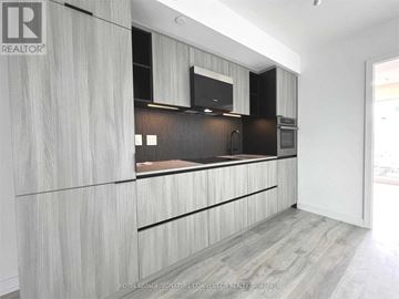 Toronto (Waterfront Communities) condo for rent - A modern kitchen with wooden cabinets and a black countertop.