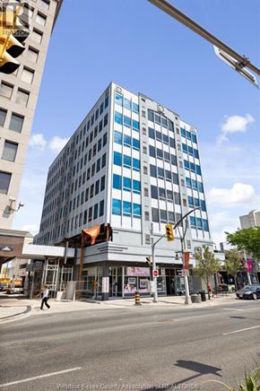 Windsor condo for rent - A tall building with a blue and white facade stands in front of a street corner.