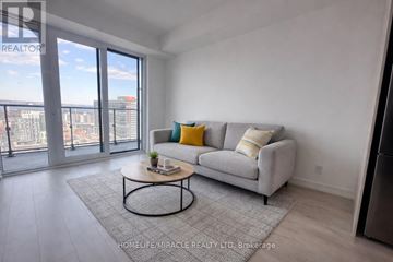 Hamilton (Corktown) condo for rent - A living room with a grey couch and a coffee table in front of a large window.
