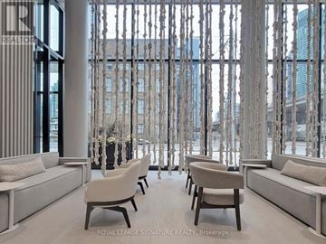Toronto (Waterfront Communities) condo for rent - A living room with white furniture and a view of a city skyline through a window.