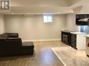Brampton (Northwest Brampton) apartment for rent - A modern living room with a black leather couch and a kitchen area with black cabinets.