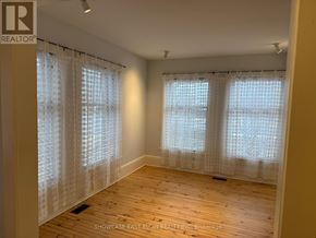 Aylmer multi-family for rent - A room with wooden floors and two windows covered with white curtains.