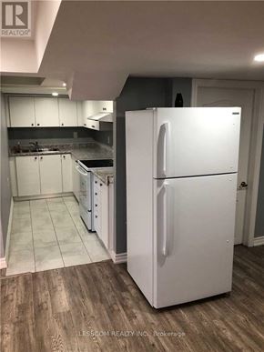 Brampton (Sandringham-Wellington) apartment for rent - A white refrigerator stands in a kitchen with wooden floors and white cabinets.
