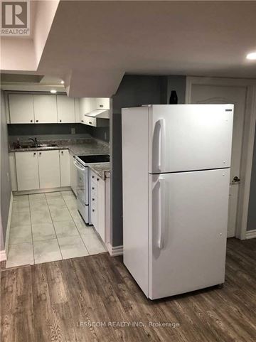 Brampton (Sandringham-Wellington) apartment for rent - A white refrigerator stands in a kitchen with wooden floors and white cabinets.