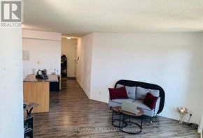 Toronto (Niagara) condo for rent - A living room with a couch, a table, and a kitchen area in the background.