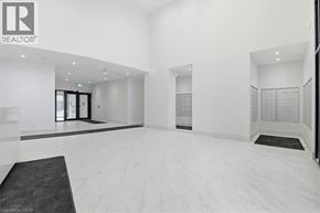 Bowmanville condo for rent - A spacious, white-walled room with a black carpet and a realtor logo on the wall.