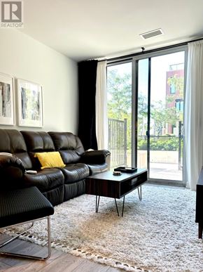 Toronto (Downsview-Roding-Cfb) condo for rent - A black leather sofa with a yellow pillow sits in a room with a large window.
