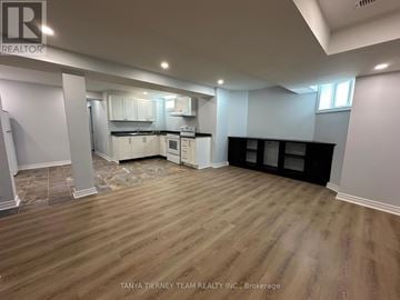 Whitby (Brooklin) apartment for rent - A room with wooden flooring and white walls, with a kitchen area in the background.