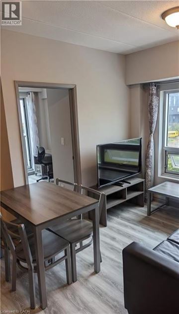 Waterloo condo for rent - A living room with a brown sofa, a wooden table and chairs, and a television.