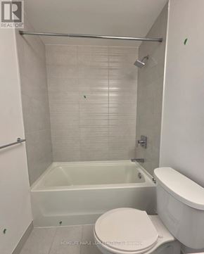 Hamilton (Corktown) condo for rent - A white toilet sits next to a bathtub in a bathroom.